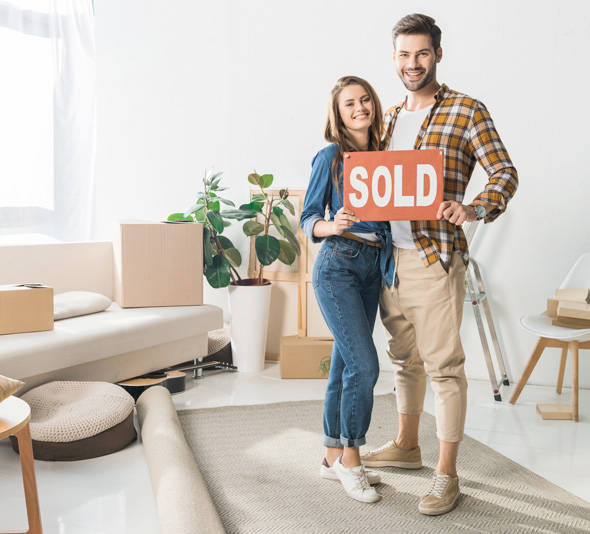 Happy couple holding sold sign in their new house
